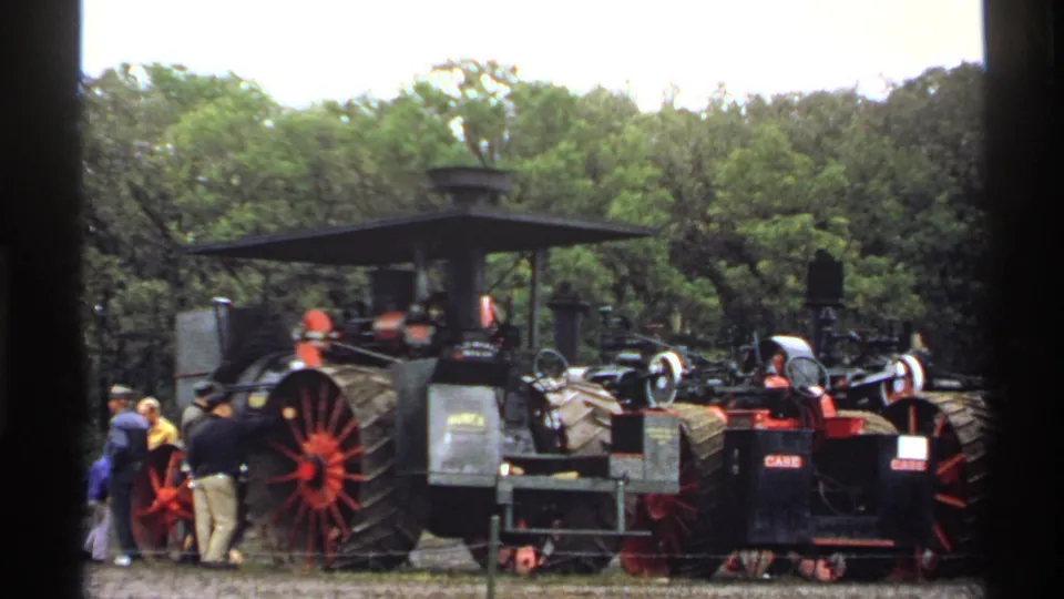 1971 Rollag, Minnesota home-movie frame showing steam tractors with large spoked wheels and visitors gathered nearby.