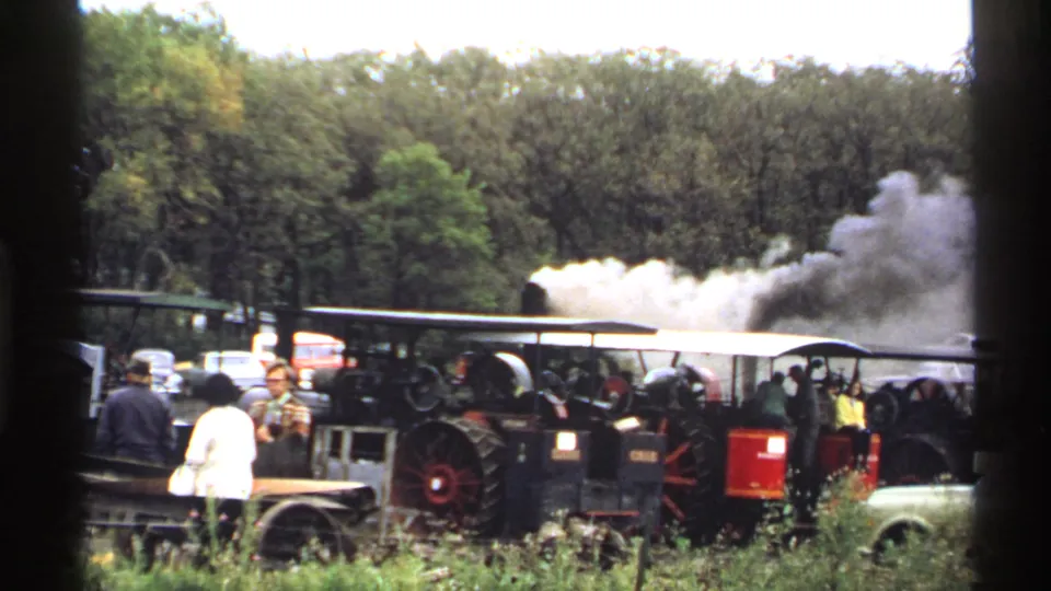 1971 Rollag, Minnesota frame with black and red steam tractors, spectators, and white steam or smoke rising near the tree line.