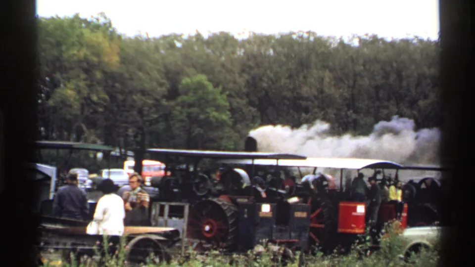 1971 Rollag, Minnesota 8mm frame showing visitors near a steam tractor display with a large white exhaust plume behind the machines.