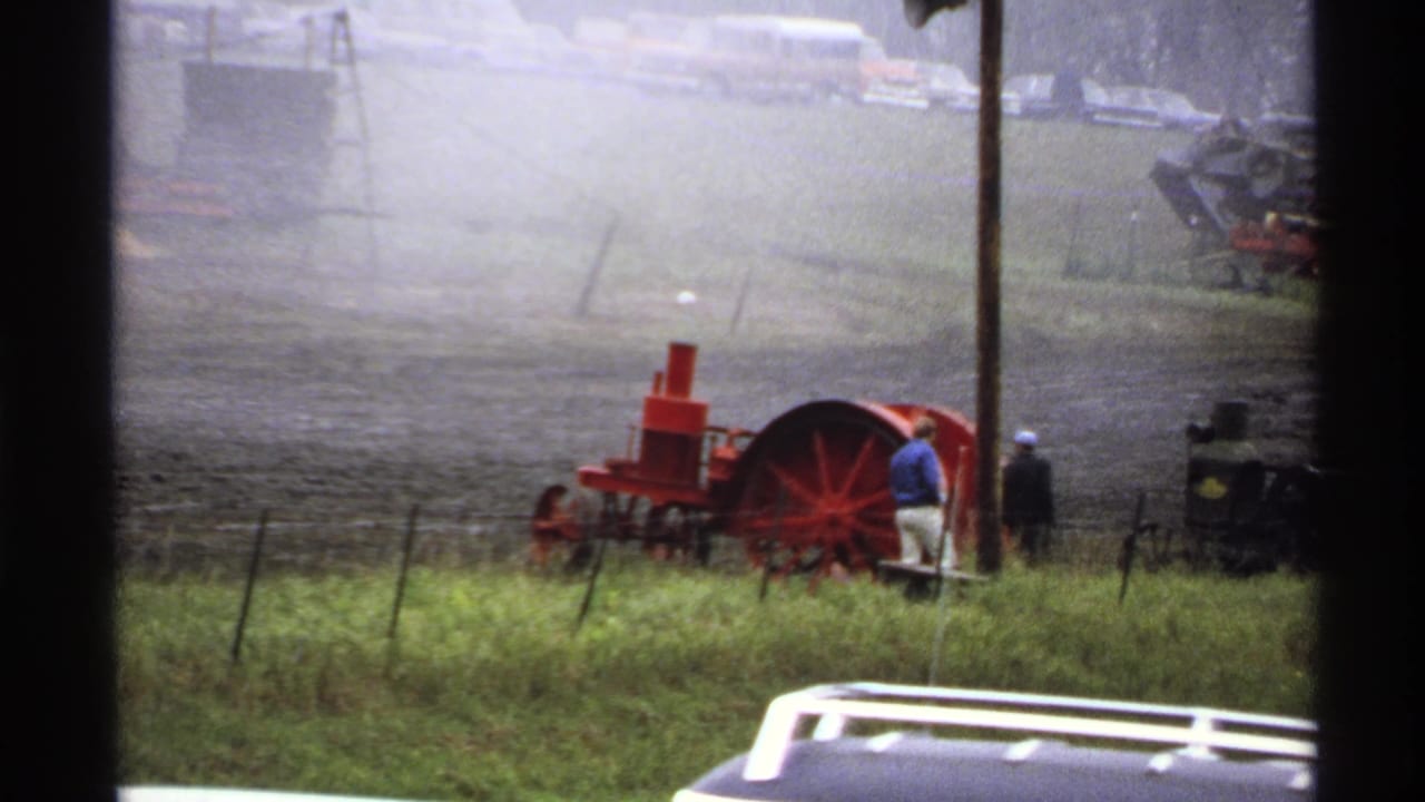 Red steam tractor in a muddy field with several onlookers nearby.