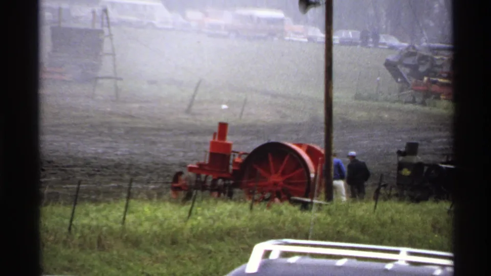 A red steam tractor and dark farm machinery appear beyond a grassy fence line during the 1971 Rollag, Minnesota rural scene.