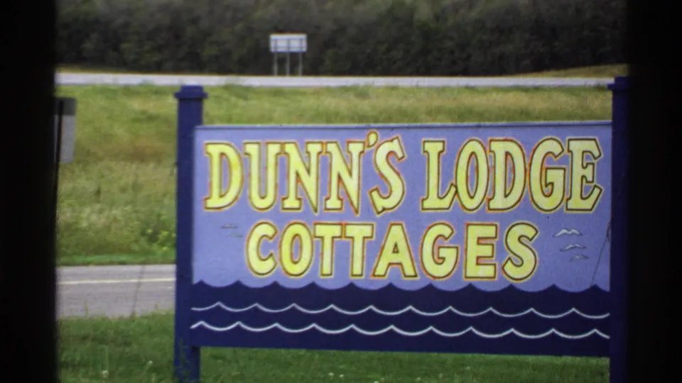 Hand-painted Dunn's Lodge Cottages roadside sign in a rural Minnesota setting, filmed on 8mm in 1971.