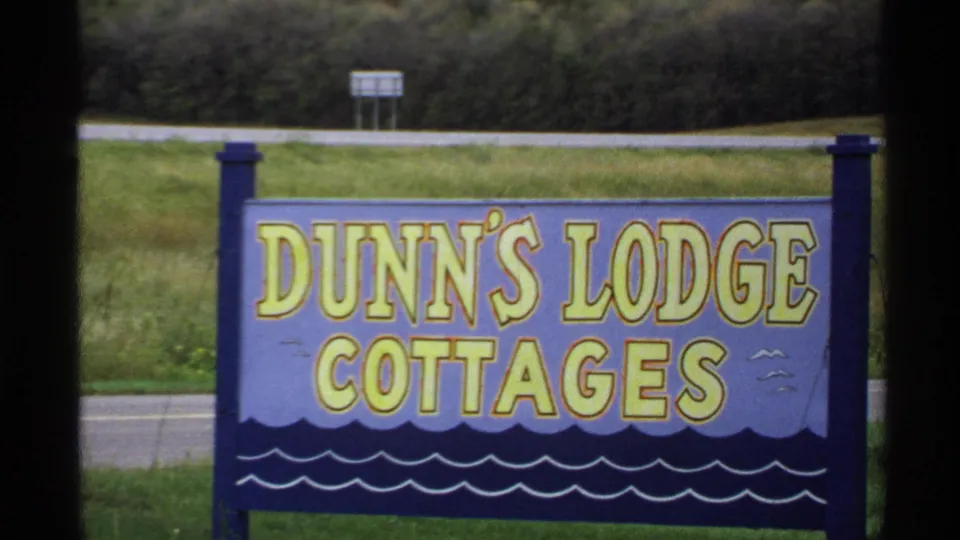1971 Rollag, Minnesota footage showing a painted Dunn's Lodge Cottages sign near grass and a roadside edge.