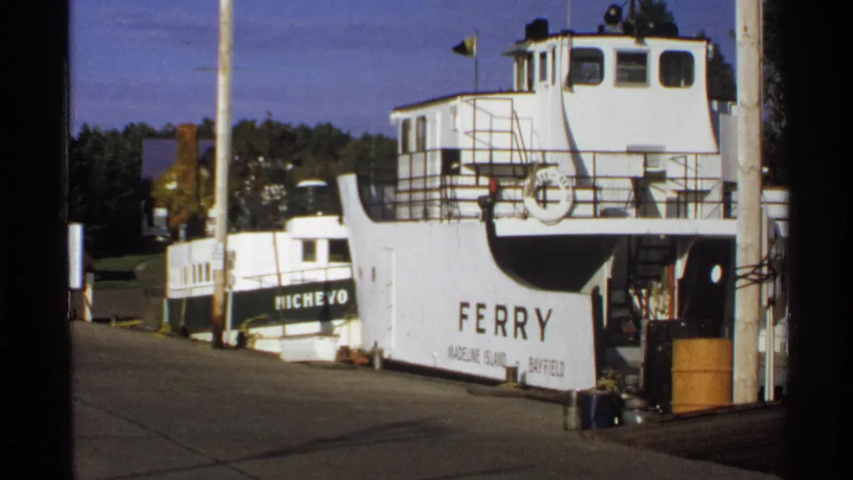 1971 home-movie view of a white Bayfield ferry at the dock, with railings, signage, poles, and trees in the background.