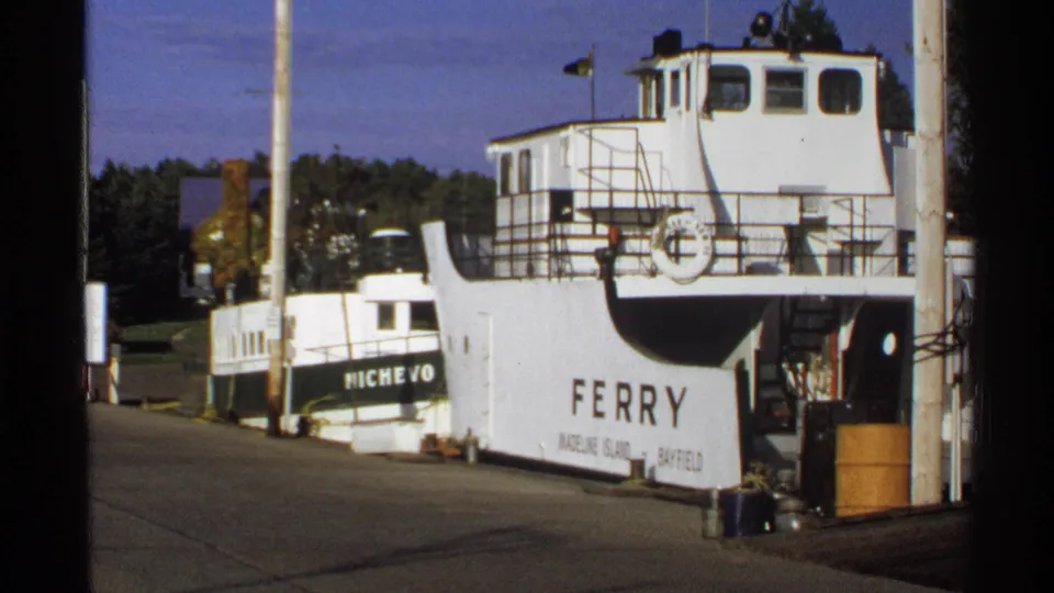 White ferry labeled for Madeline Island and Bayfield beside the smaller boat NICHEVO in a sunlit Wisconsin dock scene.