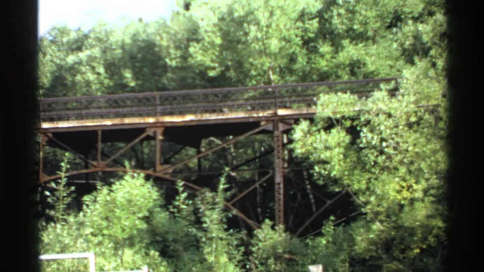 The frame holds on the metal bridge and surrounding trees, with Super 8 frame edges visible at the sides.