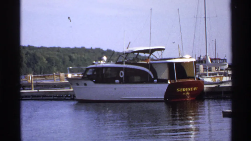 1971 Rollag, Minnesota 8mm frame showing the stern name SERENE-IV on a docked white motorboat in a marina.
