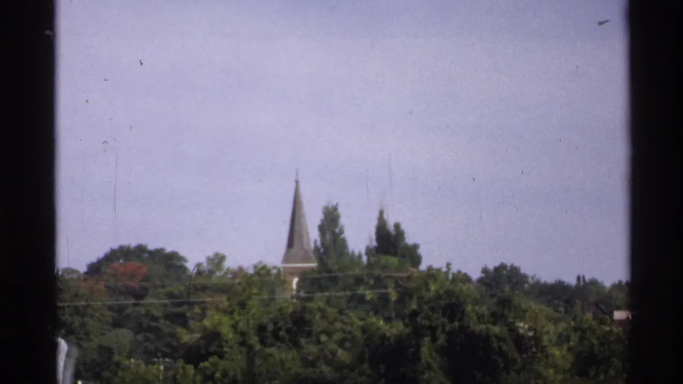 1971 Rollag, Minnesota shoreline view with dense trees and a distant church steeple visible above the harbor area.