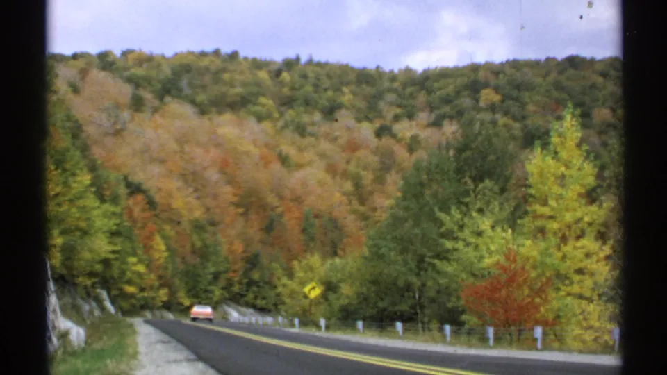 1971 Vermont road scene with a car traveling along a two-lane highway through colorful autumn trees and low wooded hills.