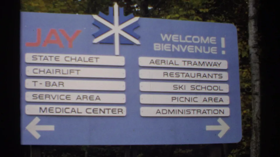 Jay resort wayfinding sign in Vermont, showing bilingual welcome text, arrows, and listed amenities including chairlift and ski school.