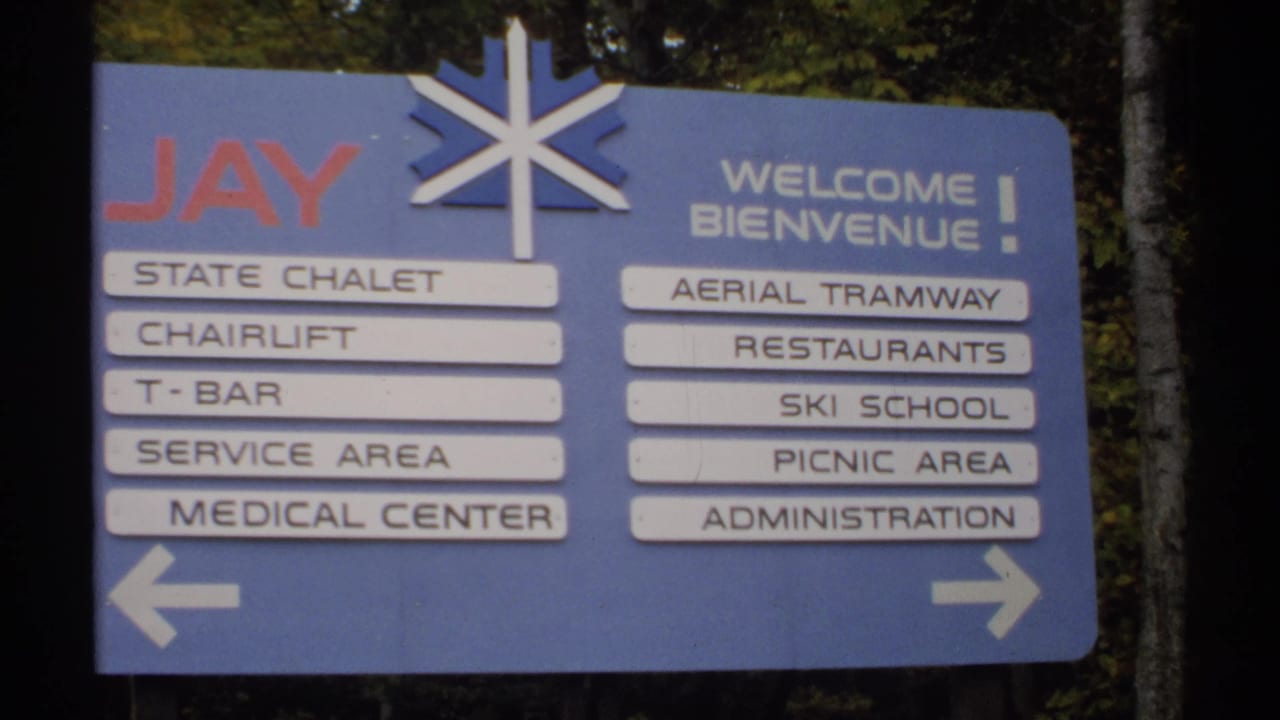 Blue Jay resort directional sign beside trees with bilingual welcome text and amenity labels.