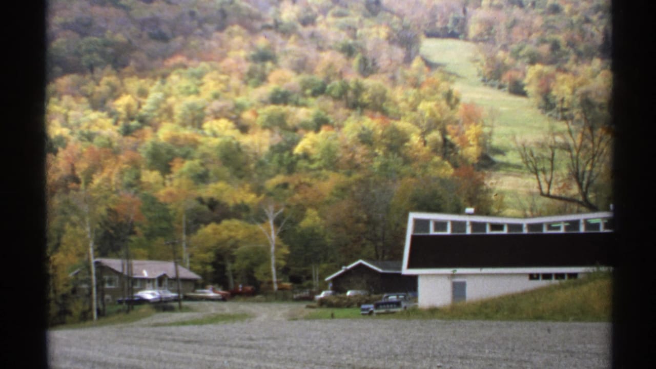 Rural buildings and parked cars at the base of an autumn hillside.