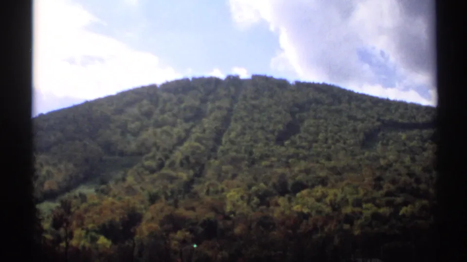 1971 Vermont home-movie view of a forested hill, mixed autumn foliage, and a partly cloudy sky.