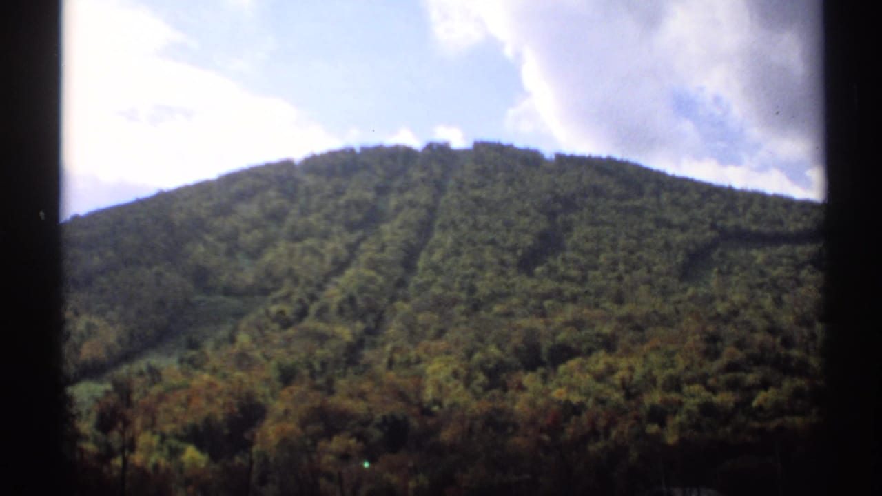 Forested mountain ridge under a partly cloudy sky, seen through dark window framing.
