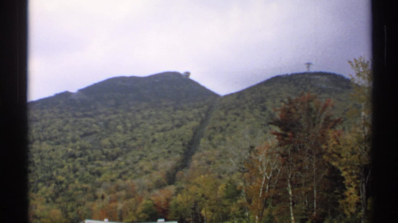 Forested Vermont mountains under an overcast sky with a summit structure visible on the ridge.