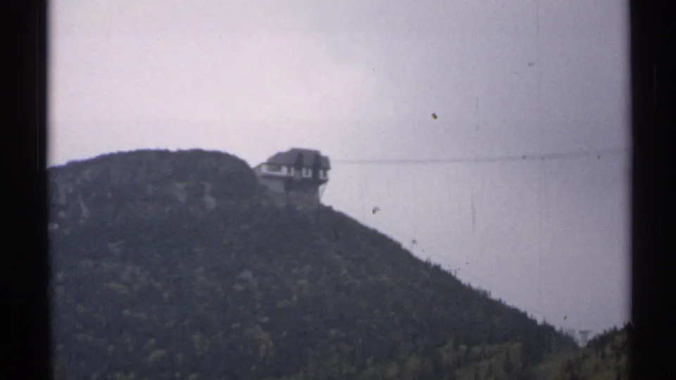 1971 Vermont 8mm view of a mountain-top tram station and cable line above a wooded ridge in overcast light.