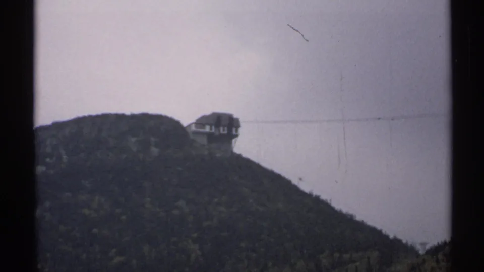 1971 Vermont 8mm frame showing a wooded mountain slope with a distant hilltop building and muted overcast sky.