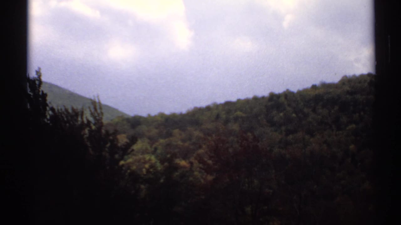 Wooded hills and a distant peak seen through dark film-frame edges beneath cloudy sky.