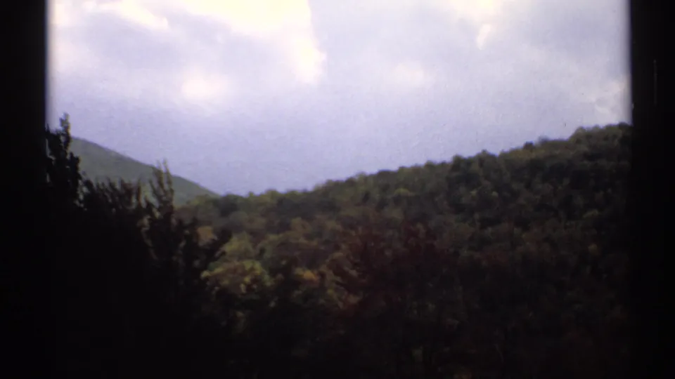 1971 Vermont 8mm view of rolling wooded hills and a distant mountain peak framed by dark exposure edges.