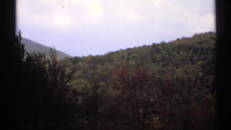 1971 Vermont 8mm frame showing layered wooded hills, a distant peak, and washed overcast sky.