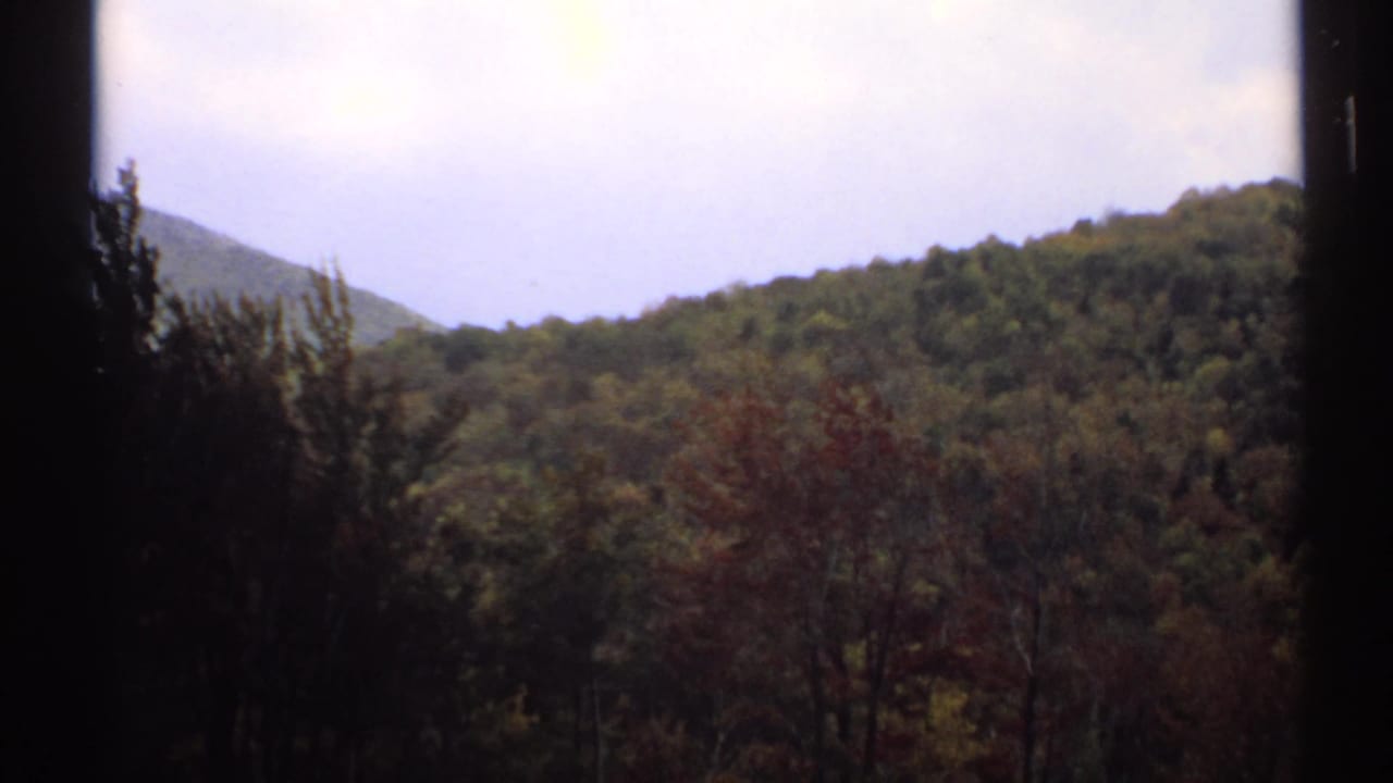 1971 Vermont 8mm view of wooded hills and autumn-toned trees framed by dark window-like edges.