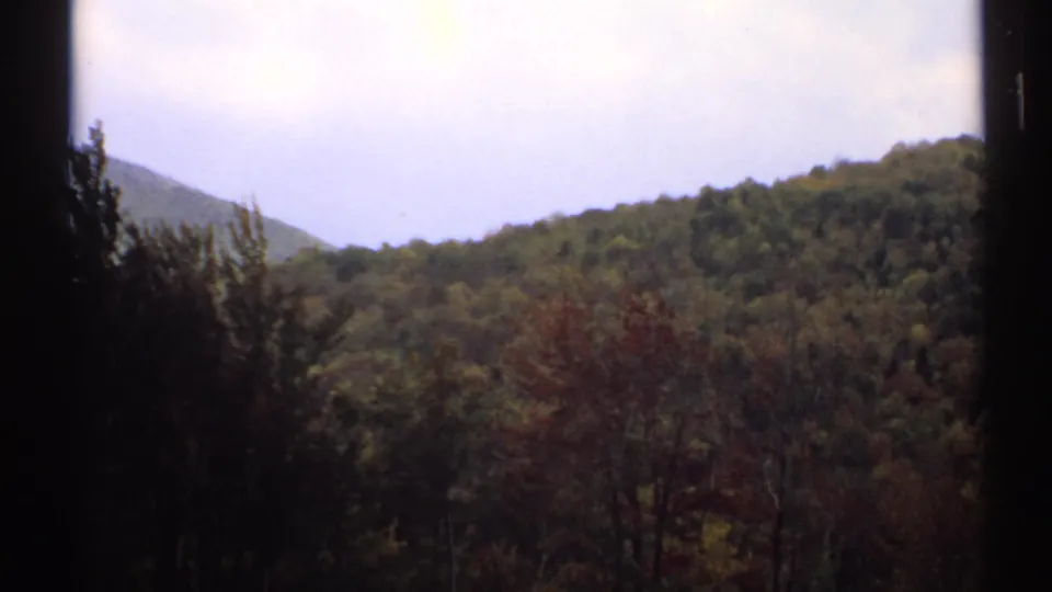 1971 Vermont 8mm view of wooded hills and autumn-toned trees framed by dark window-like edges.