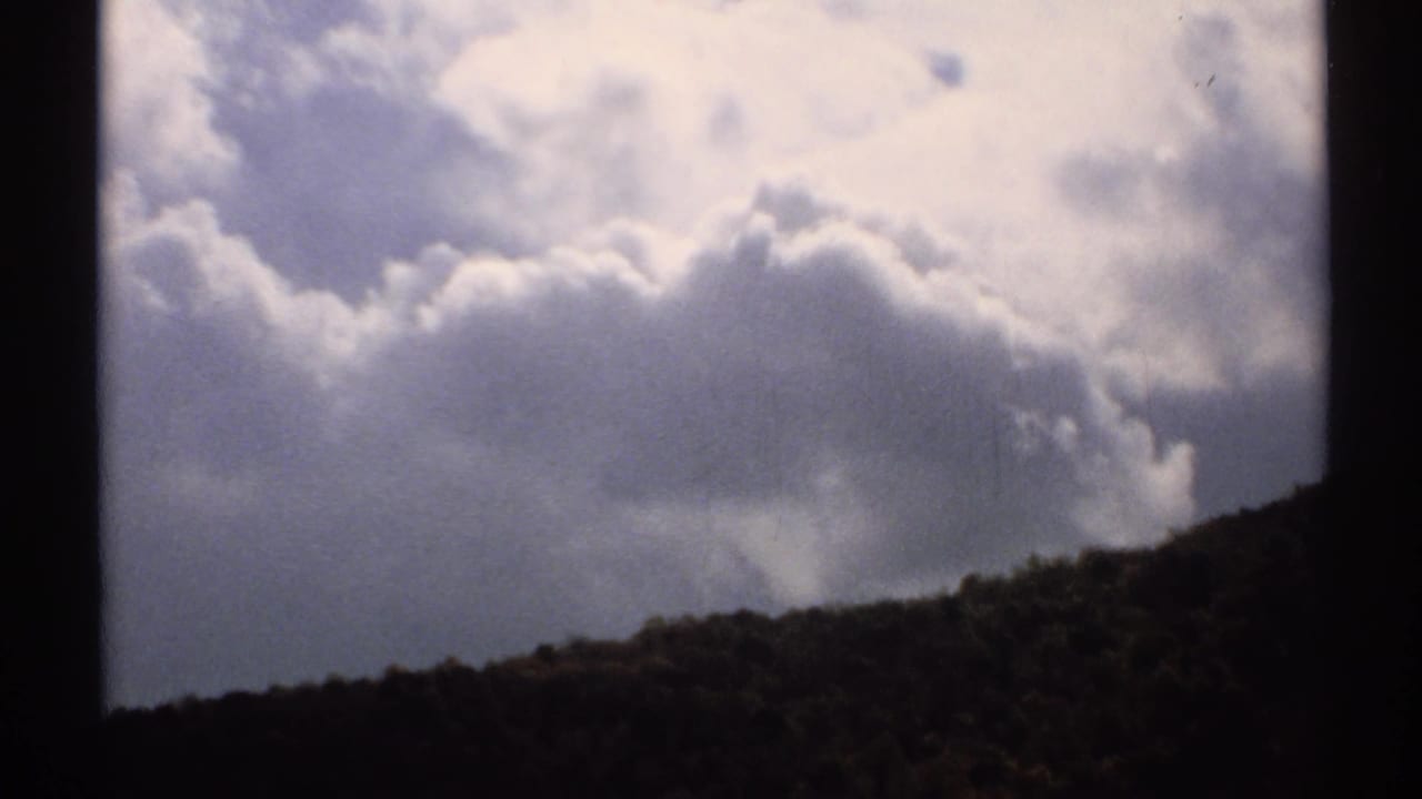 Large puffy clouds above a dark sloping hillside.