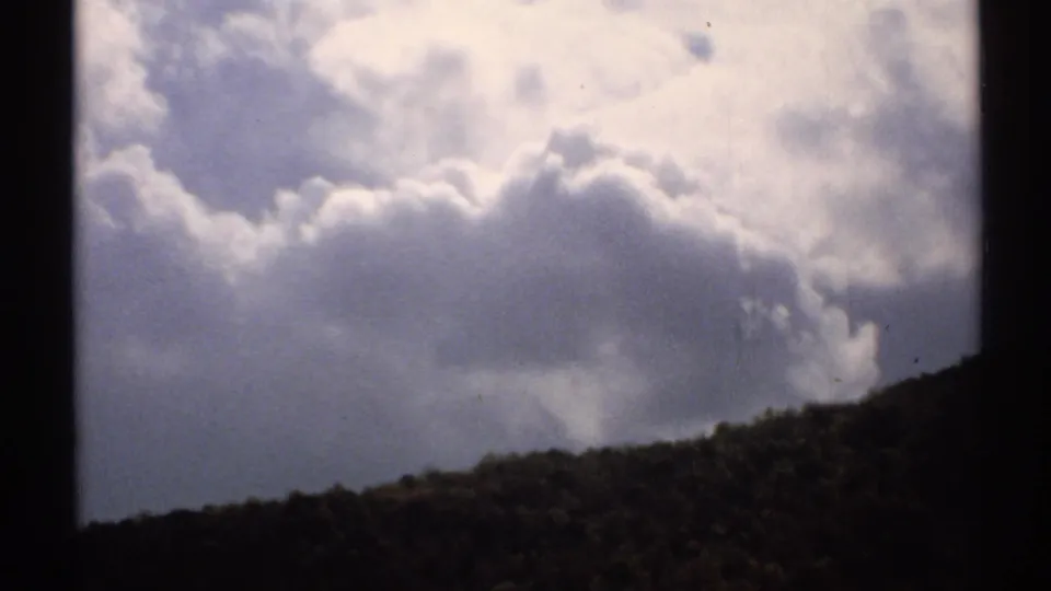 Vintage 8mm Vermont view of sunlit clouds over a low wooded ridge, with dark frame edges visible.