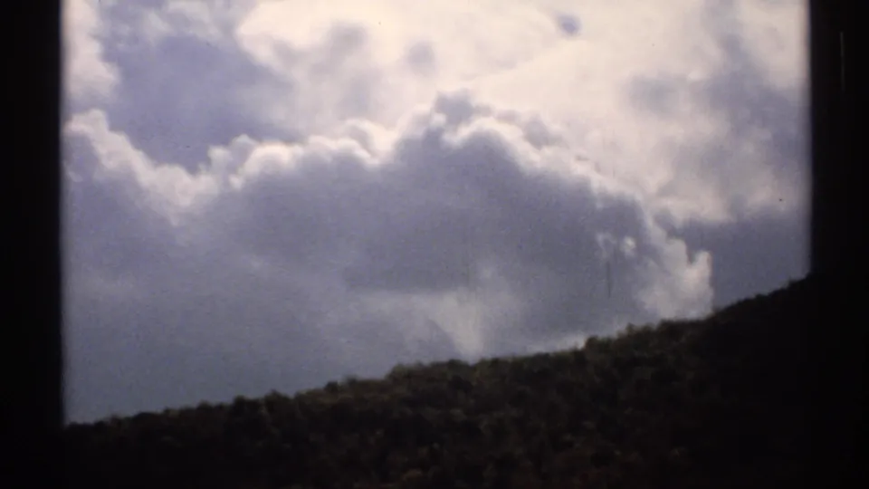 1971 Vermont 8mm frame showing puffy clouds over a shadowed hillside with visible film borders.