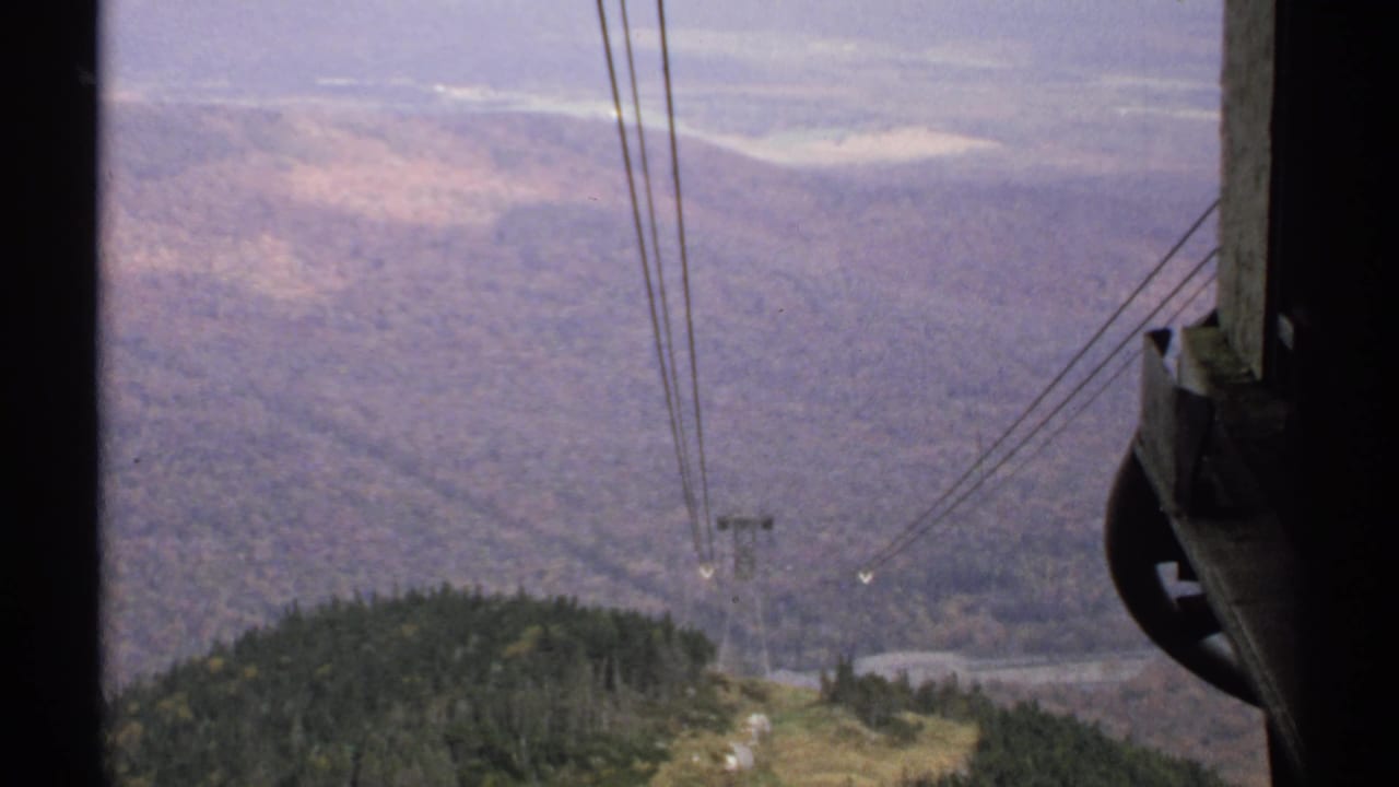 Mountain valley seen from a cable car with cables and a distant tower.