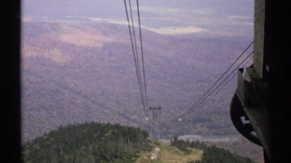 1971 Vermont cable-car view over a broad forested valley, with suspended cables and a distant support tower visible.