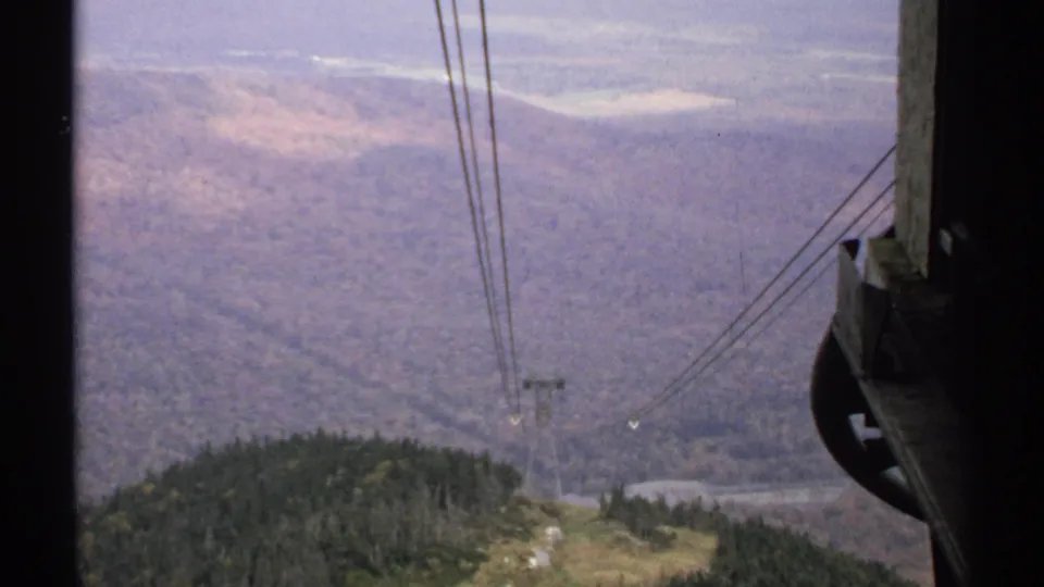 1971 Vermont 8mm view from a cable car, looking down over trees, a valley, cables, and part of the tram structure.