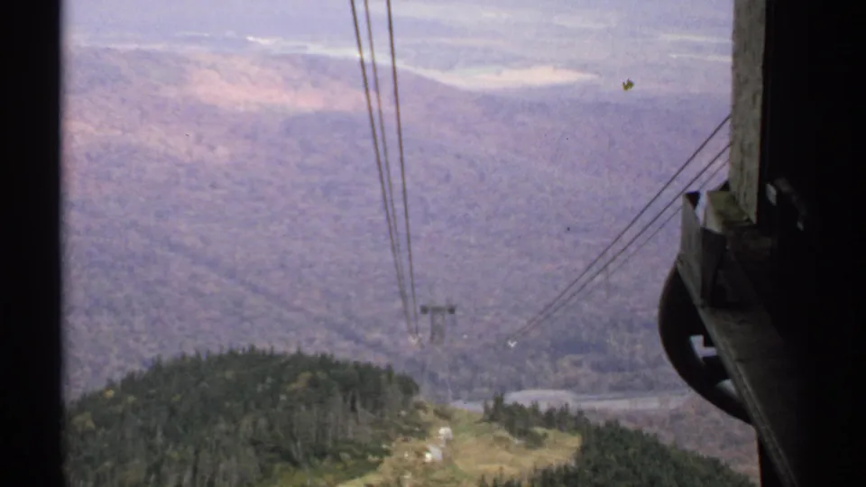 Vermont mountain tram view with cable lines, a support tower, wooded hills, and a distant valley visible through dark framing.