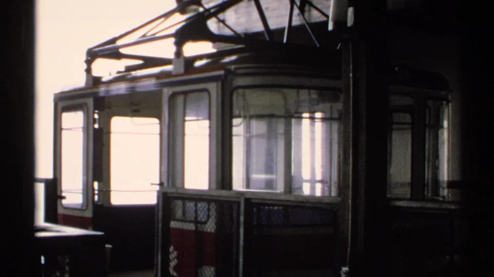 Vintage 8mm Vermont tram scene with an empty car, window panels, overhead structure, and dark station framing near the platform.