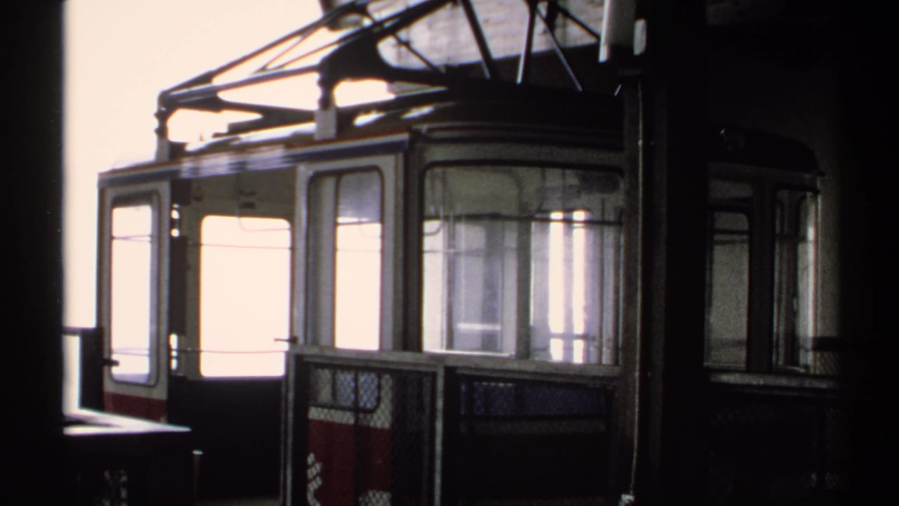 Red and white cable car cabin at a mountain station in bright daylight.