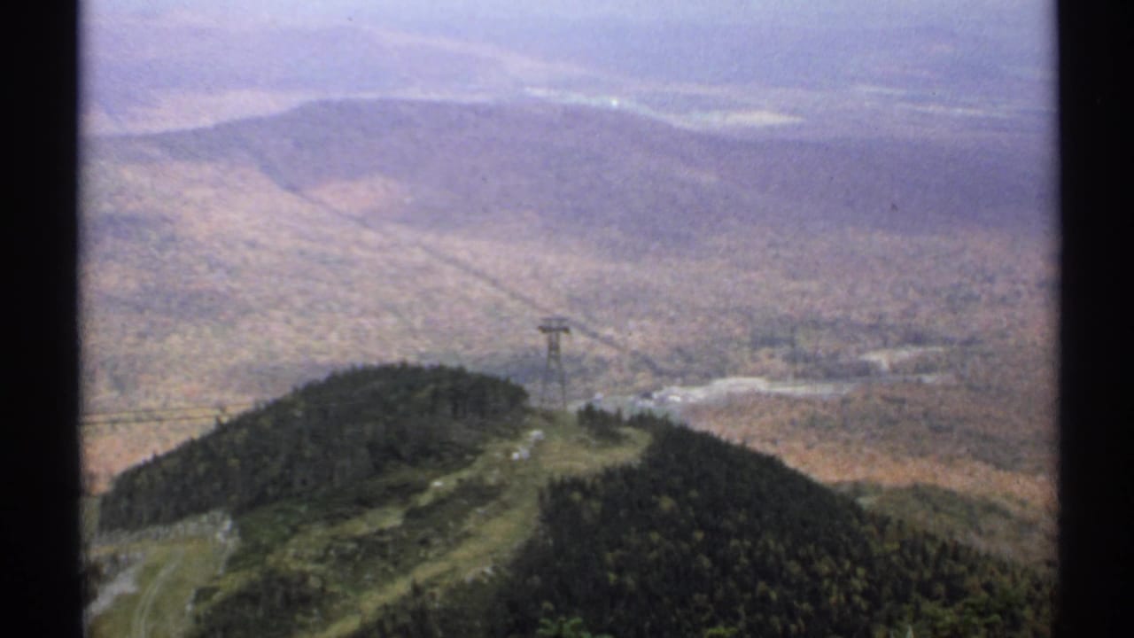 A tramway tower stands on a forested ridge above distant autumn hills.
