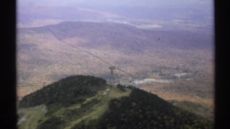 Aerial-looking 1971 Vermont view of a tramway tower on a ridge, framed by faded 8mm color and distant wooded slopes.