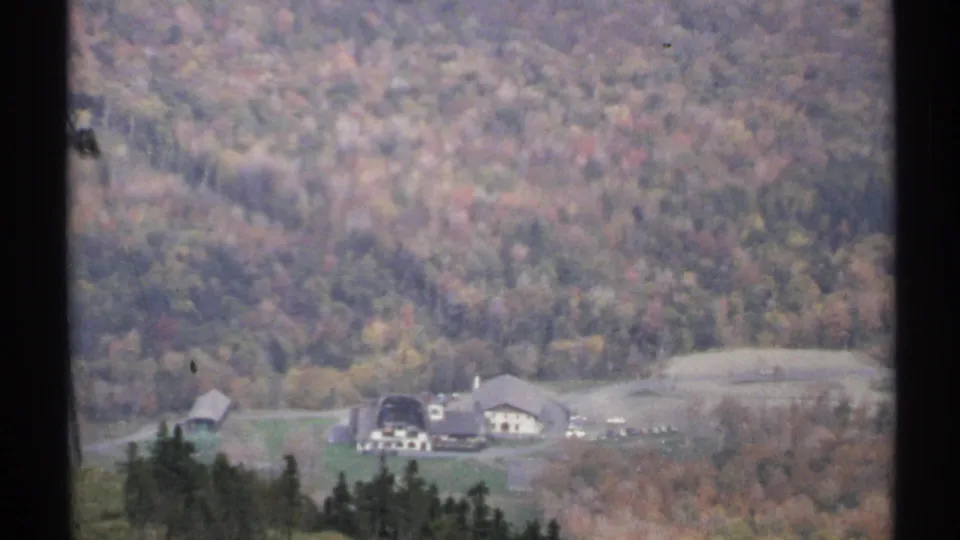 1971 Vermont 8mm frame looking down toward valley buildings, a road, and forested slopes in fall color.