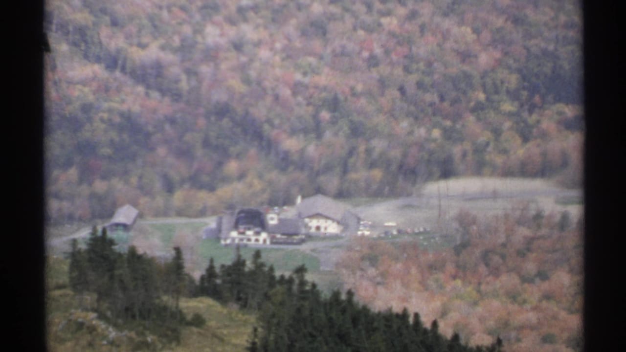 1971 Vermont aerial home-movie view of a farm cluster, open fields, and autumn hills seen through dark aircraft window framing.