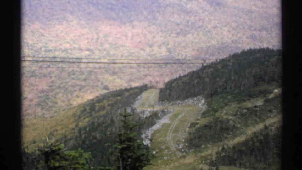 1971 Vermont 8mm overlook showing utility lines across a wooded hillside, a pale road, and a grassy mountain clearing.
