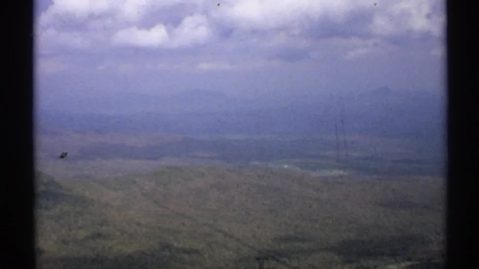 A wide Vermont mountain view shows a hazy forested valley and distant ridges beneath a cloudy sky in 8mm color footage.