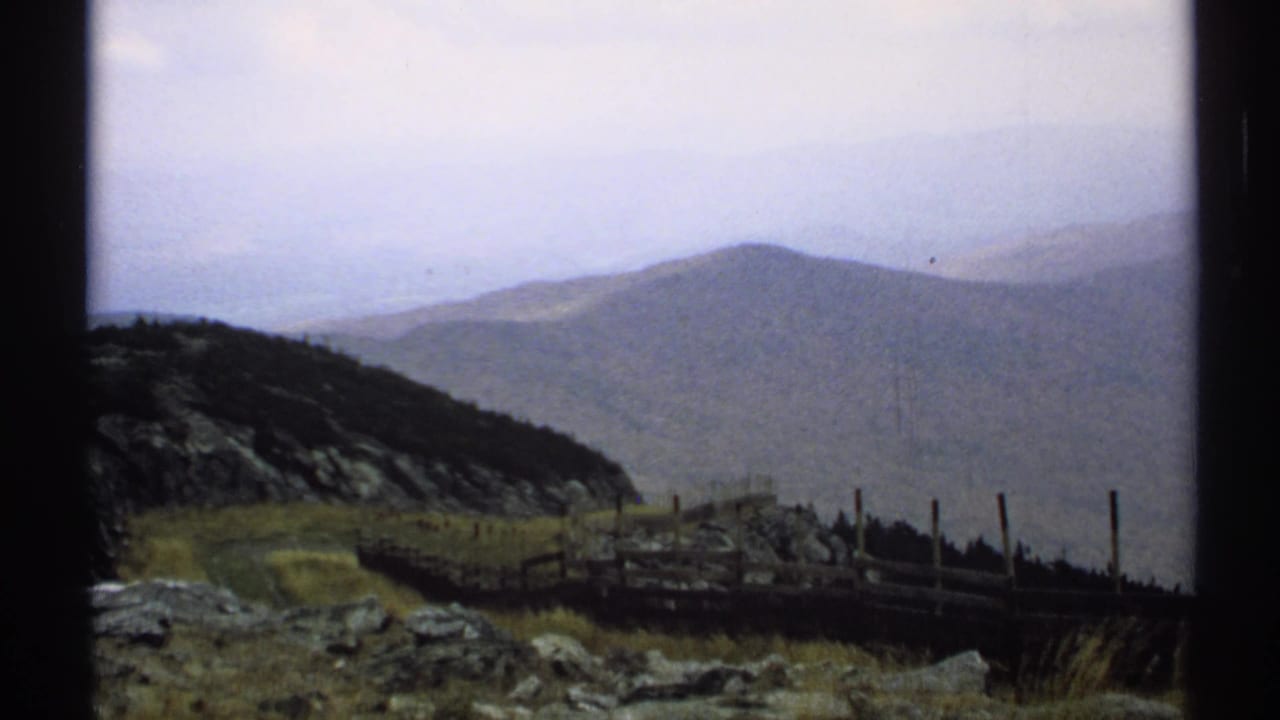 Similar mountain vista framed by dark film edges, with fence posts and rocks in front.