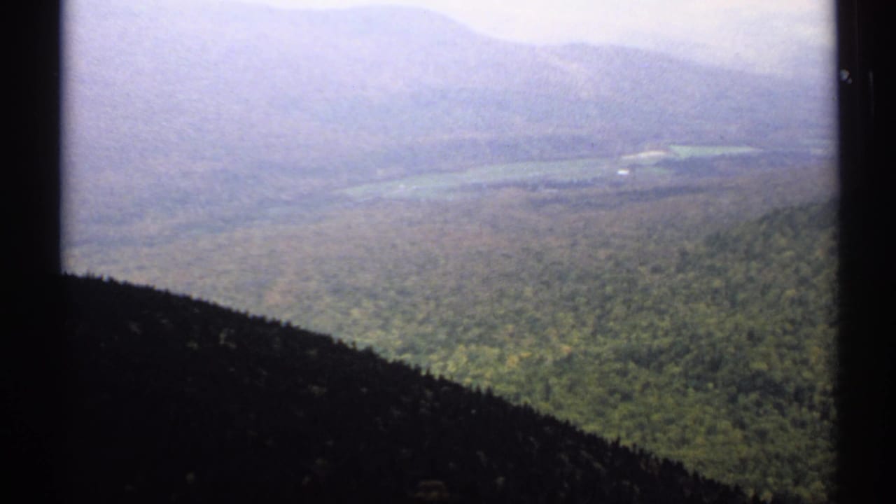 Elevated view over forested hills toward hazy mountains and a distant lake or valley.
