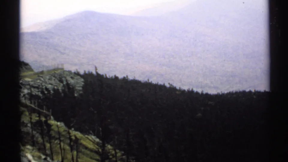 1971 Vermont 8mm frame showing a hazy mountain ridge above a dark forested foreground, with the scene partly bordered by the film frame.