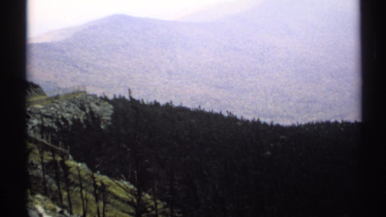 Wooded hillside and hazy mountain valley seen through dark projected film borders.