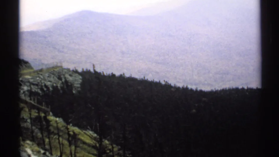 1971 Vermont 8mm frame showing a wooded slope, misty valley, and distant ridges from a high overlook.