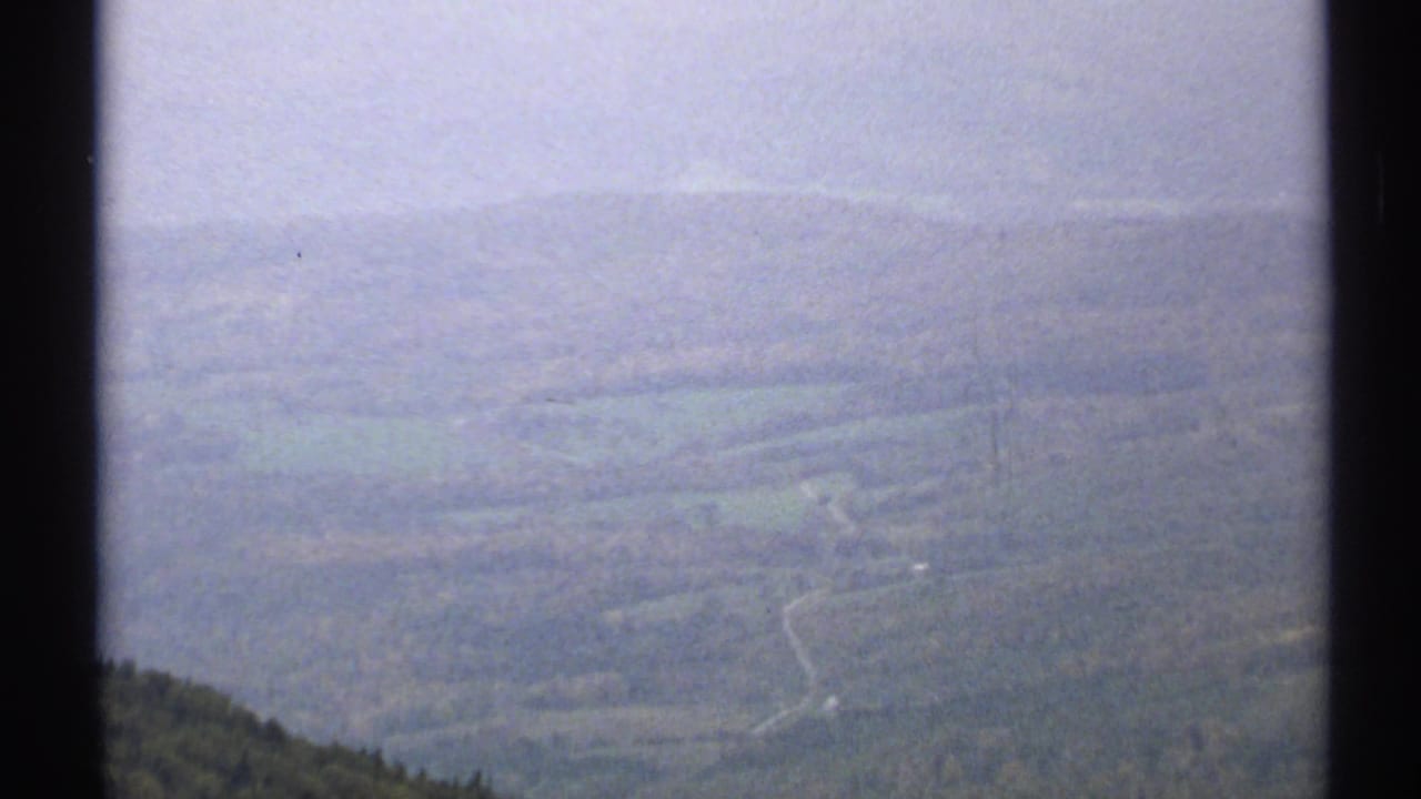 Misty valley with wooded hills and a pale winding road or trail in the distance.