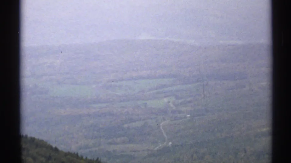 1971 Vermont 8mm view across a fog-softened valley with wooded slopes and a winding pale road or trail.