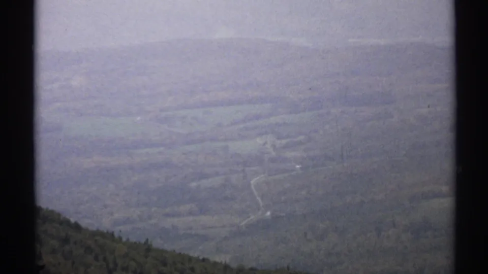 1971 Vermont 8mm frame showing a high hillside vantage over wooded valley terrain and a winding pale road or trail.