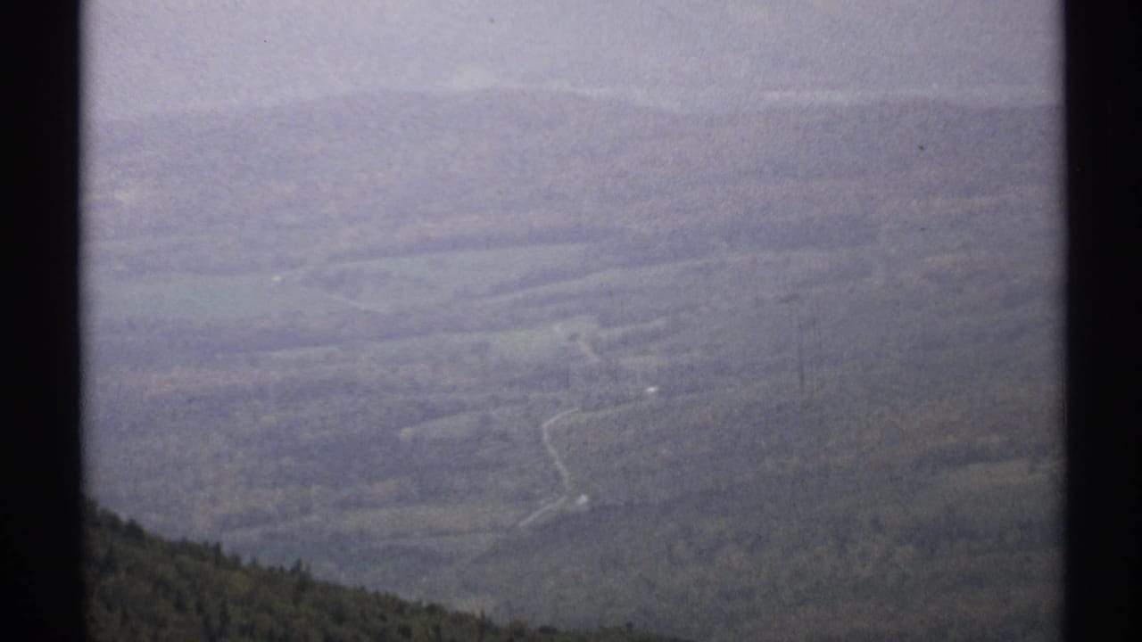 Hazy view across forested Vermont hills with a winding road in the valley below.